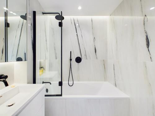 a white bathroom with a tub and a mirror at Be London - The St Pancras Residences in London