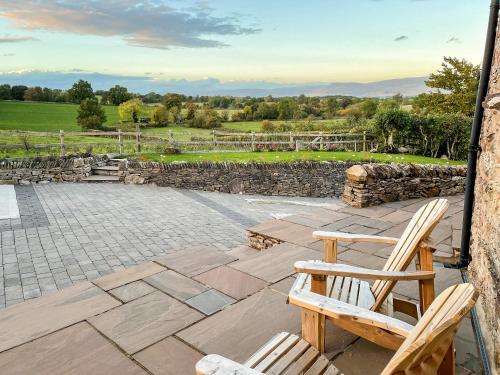 two wooden chairs sitting on a patio with a stone wall at Stallion Barn in Crosby Garrett