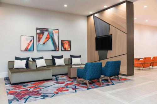 a lobby with a couch and a tv and chairs at Sonesta Hotel Grand Rapids Airport in Grand Rapids