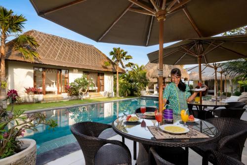 een vrouw aan een tafel voor een zwembad bij Kandahill Bali in Uluwatu