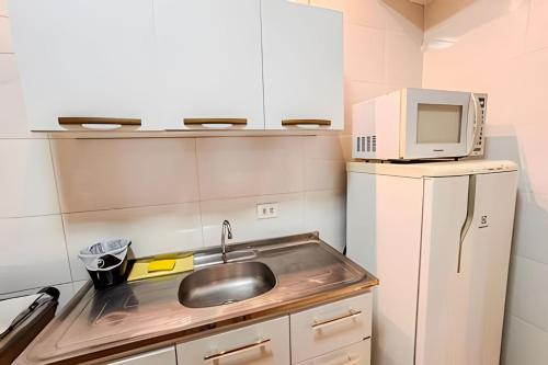 a kitchen with a sink and a microwave on top of a refrigerator at Sobrado encantador no centro, ar cond e vaga in Ourinhos