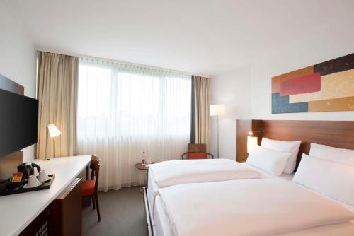 a hotel room with two beds and a desk at NH Frankfurt Niederrad in Frankfurt/Main
