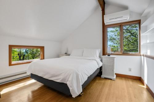 a white bedroom with a bed and two windows at House Under The Cliff in New Paltz