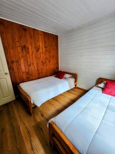 two beds in a room with wooden walls and wooden floors at Cabañas Alto del Bosque in Coñaripe