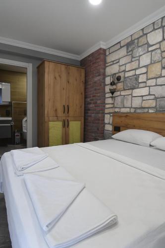 a bedroom with a white bed with a stone wall at Ballı Butik hotel in Kayakoy
