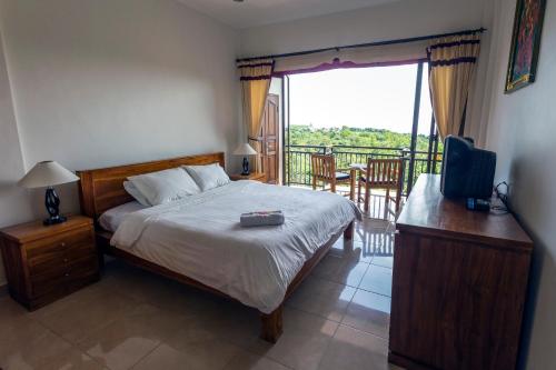 a bedroom with a bed and a television and a balcony at Waroeng Surya Home Stay in Uluwatu