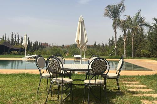 a table with chairs and an umbrella in front of a pool at Dar hamama - Villa familiale - Marrakech in El Aggada