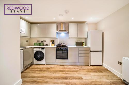 a kitchen with white cabinets and a refrigerator at Brand New Town Center, Free Fast WiFi, Balcony By Redwood Stays in Aldershot