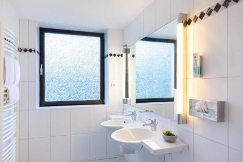 a white bathroom with two sinks and two windows at Garner Hotel Cologne East by IHG in Cologne