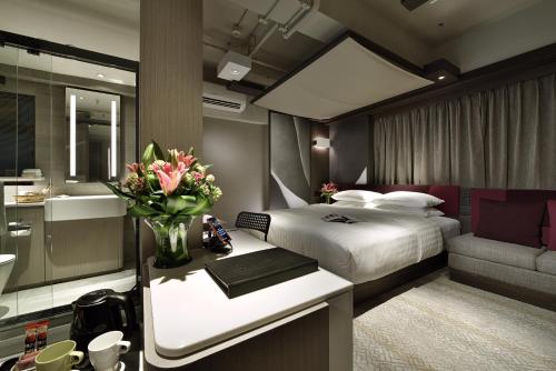 Un dormitorio con una cama y un escritorio con un jarrón de flores en Xi Hotel, en Hong Kong