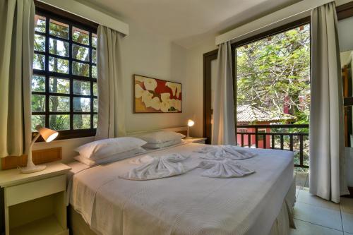 a bedroom with a large white bed with windows at Dubai Bungalows Bombinhas in Bombinhas