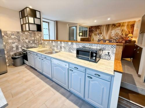 a large kitchen with blue cabinets and a microwave at Ancien moulin renove, terrasse au bord de l eau in Aurillac