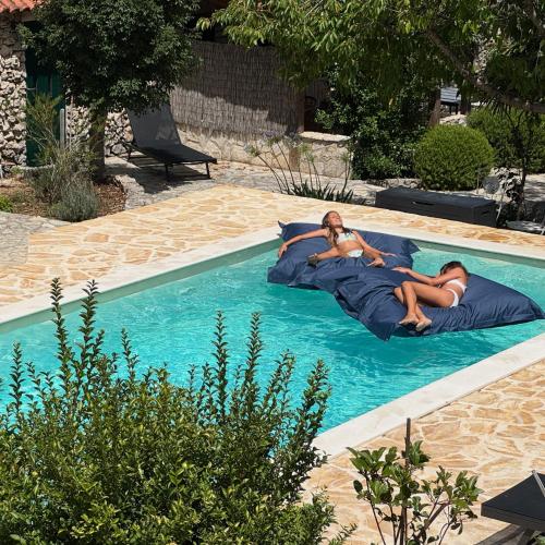two people laying on pillows in a swimming pool at Kalpic Suites & Villa in Lozovac