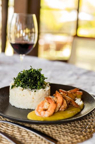 a plate of shrimp and rice with a glass of wine at Villa Côté Sud Pousada De Charme in São Miguel dos Milagres