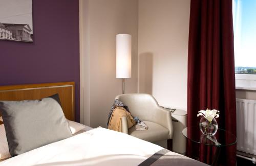 a bedroom with a bed and a chair and a window at Leonardo Hotel Karlsruhe in Karlsruhe