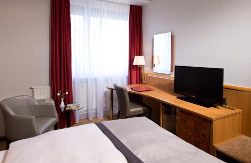 a hotel room with a bed and a desk with a television at Leonardo Hotel Karlsruhe in Karlsruhe