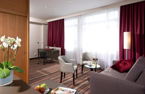 a living room with a couch and chairs and a desk at Leonardo Hotel Karlsruhe in Karlsruhe