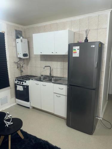 Una cocina con refrigerador negro y gabinetes blancos. en Cabañas Angeles, en Punta Arenas