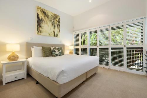 a white bedroom with a large bed and windows at East On Byron Bay Apartments in Byron Bay