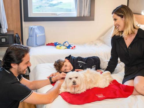 a man and woman and a child and a dog on a bed at ibis Guarapuava in Guarapuava