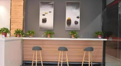 a counter with two stools in front of a counter with pictures at Shell Hotel Kaifeng Jin'an Road Bianxihu Wanda Plaza in Kaifeng