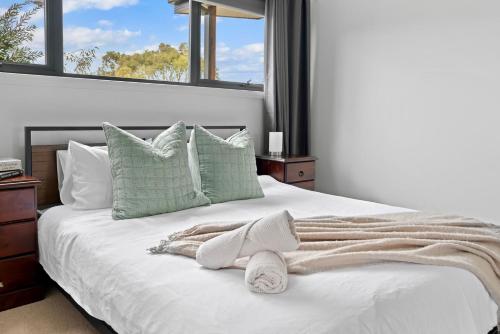 a white bed with green pillows and a blanket at Tea Tree Pool Retreat in Inverloch