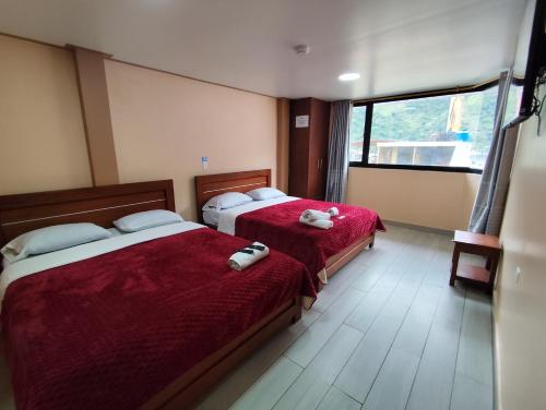 a bedroom with two beds with red sheets and a window at Hostal California AC-DC in Baños