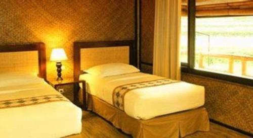 two beds in a hotel room with a window at Sambi Resort, Spa & Resto in Yogyakarta