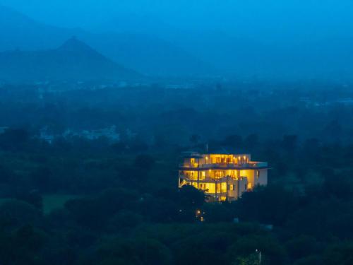 a building with lights on in the middle of a forest at Dilip Niwas in Udaipur