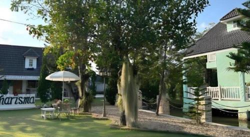 a house with a tree and an umbrella in a yard at Charisma Resort in Ratchaburi