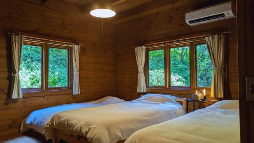 two beds in a room with two windows at 自然豊かな森の中に静かに佇むログハウス #貸別荘 #一棟貸切 #グループ旅行や家族旅行におすすめ #広々吹き抜けリビング #BBQのできるウッドデッキ #ジブリ風空間 #満天の星空 #鋸南 #南房総 #komorebi in Kyonan