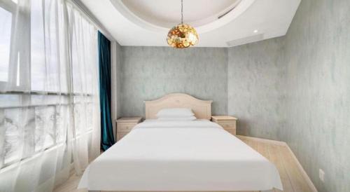 a bedroom with a white bed and a chandelier at Vienna Hotel Guiyang Jiaxiulou Jichang Road in Guiyang