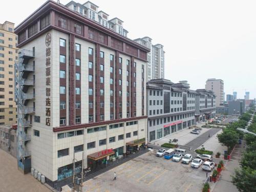 a tall building with cars parked in a parking lot at GreenTree Inn Jinzhong PinGYAo City South Railway Station Express Hotel in Pingyao