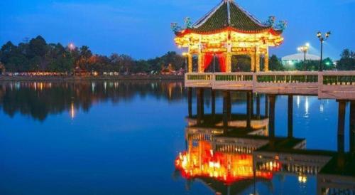 a pagoda in the middle of a lake at night at Maximize Brand New Hostel Udonthani in Udon Thani