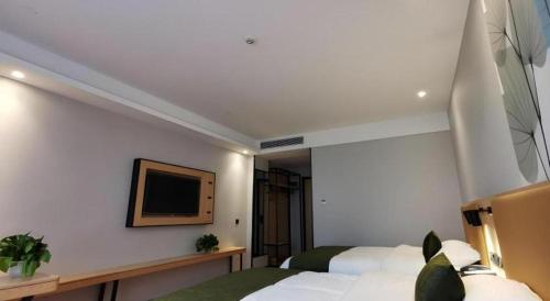 a bedroom with two beds and a tv on the wall at GreenTree Inn Ganzhou Gan County Bus Station in Ganzhou
