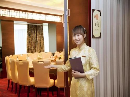a woman standing in a dining room holding a book at Huangshan Shuguang Yusong Hotel in Huangshan