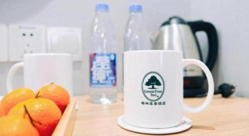 a white coffee mug sitting on a table with fruit at GreenTree Inn Jiaxing Tongxiang Tudian Express Hotel in Jiaxing