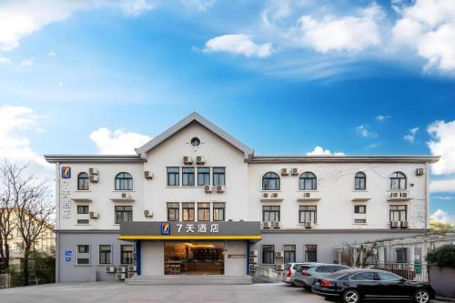 a large white building with cars parked in a parking lot at 7 Days Inn Qingdao Liaoyang West Road Xinye Plaza Metro Station in Qingdao