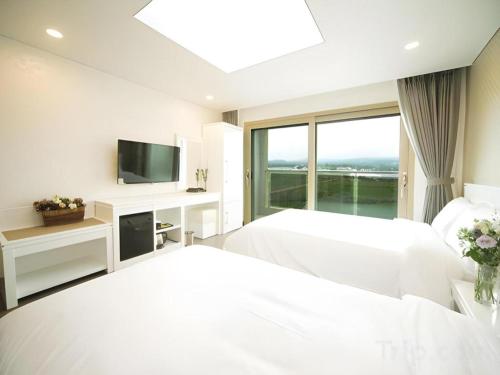 a white bedroom with two beds and a tv at Sea View Hotel in Jeju