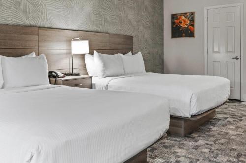 two beds in a hotel room with white sheets at University Park Inn & Suites, an Ascend Collection Hotel in Davis