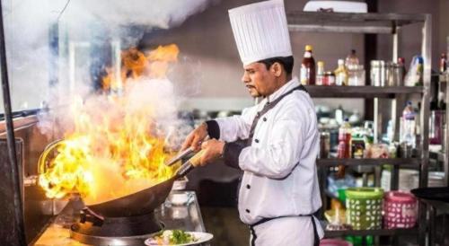 a chef cooking food in a wok in a kitchen at Hotel Gajur Palace in Itahari