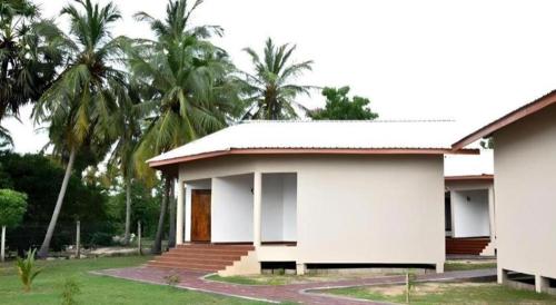 a small white house with palm trees in the background at Naaval Hotel in Batticaloa