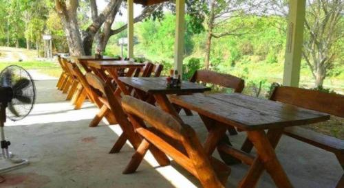 a row of wooden tables and chairs with a fan at At Home Suanphung in Ratchaburi