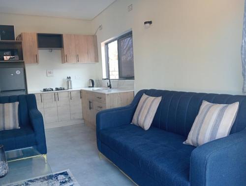a living room with a blue couch and a kitchen at Cosy One bedroom with good Solar backup & Wi-Fi in Lusaka