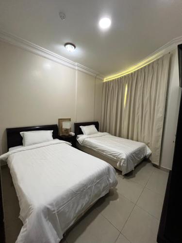 Dos camas en una habitación de hotel con sábanas blancas. en Aldaar apartments, en Al Bukayriyah
