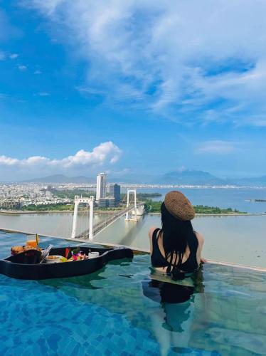 a woman sitting in a infinity pool with a boat in the water at Gold Apartment With Sea View In Da Nang Bay in Da Nang