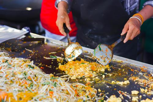 a person cooking food on a grill with spoons at The Hidden Khaosan เดอะ ฮิดเด้นข้าวสาร in Bang Bua Thong Railway Station