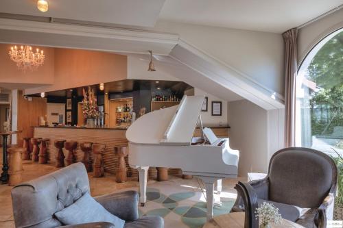 a white piano in a living room with a bar at Hotel Mercure Parc du Coudray - Barbizon in Le Coudray-Montceaux