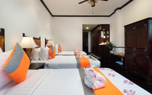 a bedroom with three beds with orange and white pillows at Le Grande Indochine Hotel in Siem Reap