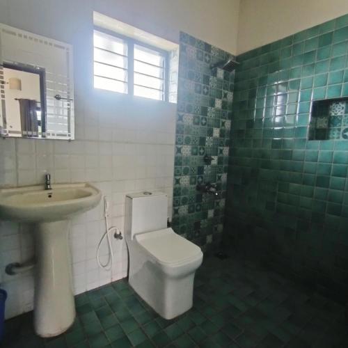 a green tiled bathroom with a toilet and a sink at Mad about Coco Yoga & Beach Retreat in Varkala